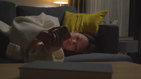 Woman-Spending-Evening-At-Home-Lying-On-Sofa-With-Mobile-Phone-Scrolling-Through-Internet-Or-Social-Media-7